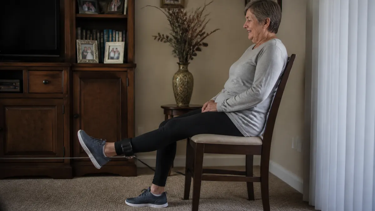 Ankle straps wrapped around a person's legs as they do a seated leg extension in a living room chair
